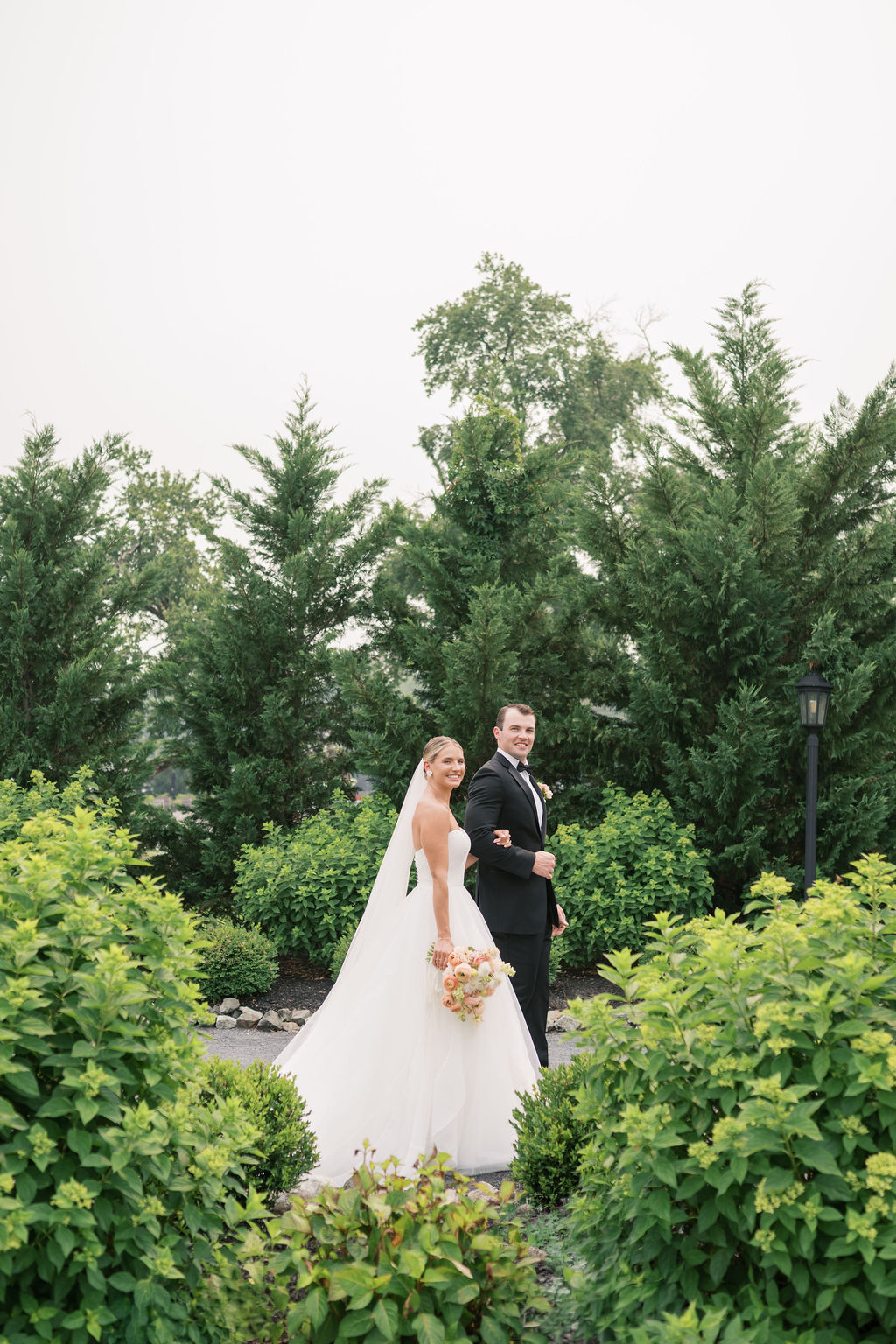 Bride and Groom hold hands, walk through gardens at Glen Foerd